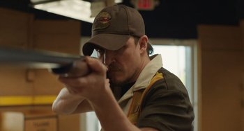 Movie still from “The Passenger” (2023), directed by Carter Smith – A man in a hat is holding a gun; Close Up shot, Low angle
