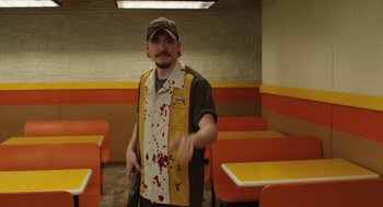 Movie still from “The Passenger” (2023), directed by Carter Smith – A man in a restaurant with blood on his shirt; Medium shot, High angle