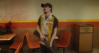 Movie still from “The Passenger” (2023), directed by Carter Smith – A man holding a gun in a room with chairs; Medium shot, Low angle