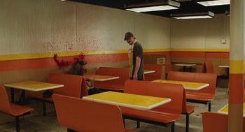 Movie still from “The Passenger” (2023), directed by Carter Smith – A man standing in front of a bunch of orange tables; Wide shot, High angle