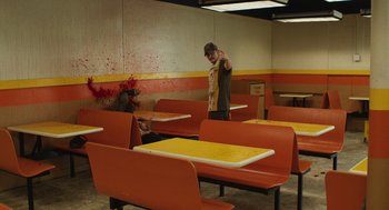Movie still from “The Passenger” (2023), directed by Carter Smith – Two people are sitting at a table in an empty restaurant; Wide shot, High angle