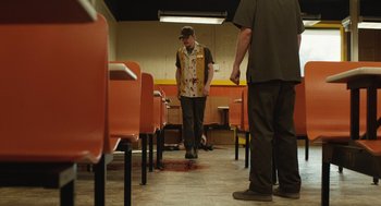 Movie still from “The Passenger” (2023), directed by Carter Smith – A man standing in front of a bunch of chairs; Wide shot, Low angle