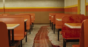 Movie still from “The Passenger” (2023), directed by Carter Smith – A row of chairs in a room with a rug on the floor; Wide shot, High angle