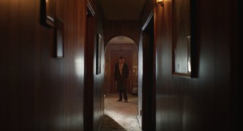 Movie still from “The Passenger” (2023), directed by Carter Smith – A man standing in a hallway in front of an archway; Wide shot, Low angle