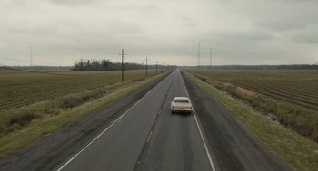 Movie still from “The Passenger” (2023), directed by Carter Smith – A car driving down the middle of a road; Extreme Wide shot, High angle