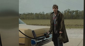 Movie still from “The Passenger” (2023), directed by Carter Smith – A man standing in front of a car with a gas pump; Medium shot, Over the shoulder angle