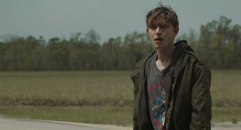 Movie still from “The Passenger” (2023), directed by Carter Smith – A young man standing on the side of a road; Medium shot, Over the shoulder angle