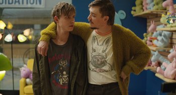 Movie still from “The Passenger” (2023), directed by Carter Smith – Two young men standing next to each other in front of a wall; Medium shot, Over the shoulder angle