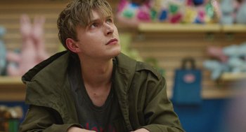Movie still from “The Passenger” (2023), directed by Carter Smith – A young man sitting in a room looking up; Close Up shot, Over the shoulder angle