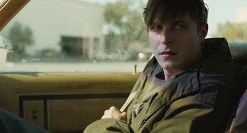 Movie still from “The Passenger” (2023), directed by Carter Smith – A man sitting on a bench in the rain; Close Up shot, Over the shoulder angle
