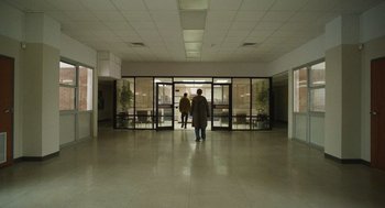Movie still from “The Passenger” (2023), directed by Carter Smith – Two people are walking through an open door way; Extreme Wide shot, Low angle