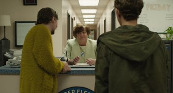 Movie still from “The Passenger” (2023), directed by Carter Smith – A woman sitting in front of two men in front of a counter; Medium shot, Over the shoulder angle
