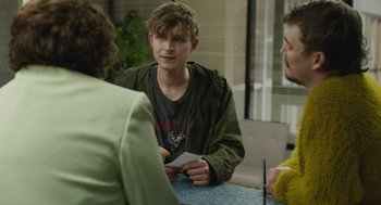 Movie still from “The Passenger” (2023), directed by Carter Smith – A group of people sitting around a table; Medium shot, Over the shoulder angle