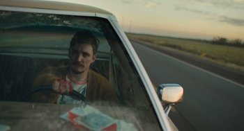 Movie still from “The Passenger” (2023), directed by Carter Smith – A man sitting in the driver's seat of a car on the side of the road; Medium shot, Over the shoulder angle