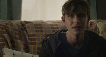 Movie still from “The Passenger” (2023), directed by Carter Smith – A man sitting on top of a couch in front of a window; Close Up shot, Over the shoulder angle