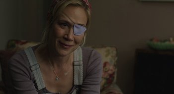 Movie still from “The Passenger” (2023), directed by Carter Smith – A woman with a eye patch sitting on a couch; Close Up shot, Over the shoulder angle