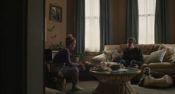 Movie still from “The Passenger” (2023), directed by Carter Smith – Two people are sitting in a living room; Wide shot, Over the shoulder angle