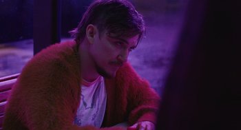 Movie still from “The Passenger” (2023), directed by Carter Smith – A man in a red jacket is sitting in a purple light; Close Up shot, Over the shoulder angle
