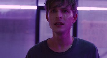 Movie still from “The Passenger” (2023), directed by Carter Smith – A young man in a black shirt is looking at the camera; Close Up shot, Over the shoulder angle