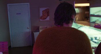 Movie still from “The Passenger” (2023), directed by Carter Smith – A woman in a red sweater is looking at a picture on the wall; Medium shot, Over the shoulder angle