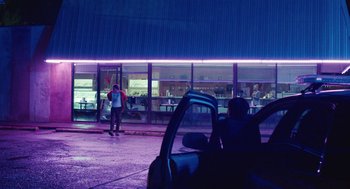 Movie still from “The Passenger” (2023), directed by Carter Smith – A person standing in front of a building at night; Wide shot, Low angle