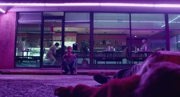 Movie still from “The Passenger” (2023), directed by Carter Smith – A man sitting on the ground in front of a building; Wide shot, Low angle