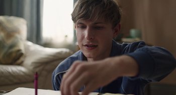 Movie still from “The Passenger” (2023), directed by Carter Smith – A man sitting at a table looking down at a piece of paper; Close Up shot, Over the shoulder angle