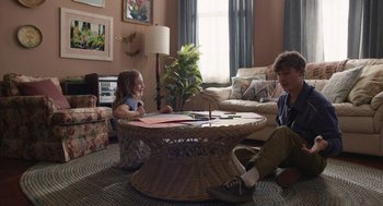 Movie still from “The Passenger” (2023), directed by Carter Smith – Two children sitting on the floor in a living room; Wide shot, Over the shoulder angle