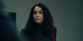 Movie still from “Dopesick” (2021), directed by Danny Strong – A woman with long black curly hair wearing a purple jacket; Close Up shot, Over the shoulder angle