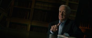 Movie still from “The Pigeon Tunnel” (2023), directed by Errol Morris – An older man is sitting at a table in front of books; Close Up shot, Over the shoulder angle
