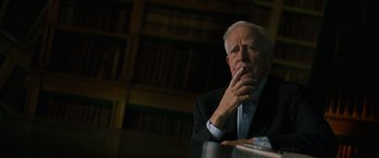 Movie still from “The Pigeon Tunnel” (2023), directed by Errol Morris – An older man sitting in front of a book shelf; Close Up shot, Low angle