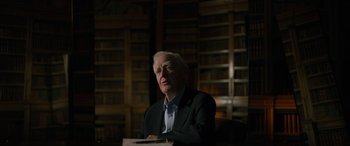 Movie still from “The Pigeon Tunnel” (2023), directed by Errol Morris – An older man sitting in front of a book shelf; Medium shot, Low angle