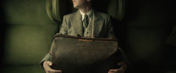Movie still from “The Pigeon Tunnel” (2023), directed by Errol Morris – A man in a suit and tie holding a suit case; Medium shot, High angle