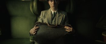 Movie still from “The Pigeon Tunnel” (2023), directed by Errol Morris – A man in a suit and hat holding a suit case; Medium shot, Overhead angle