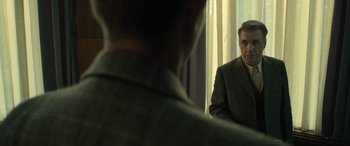 Movie still from “The Pigeon Tunnel” (2023), directed by Errol Morris – A man in a suit looking at himself in the mirror; Close Up shot, Over the shoulder angle