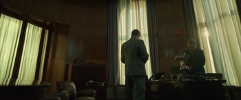 Movie still from “The Pigeon Tunnel” (2023), directed by Errol Morris – A man standing in front of a window in a living room; Wide shot, Low angle
