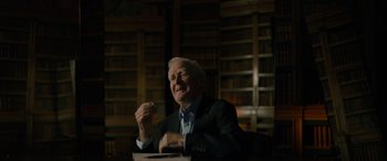 Movie still from “The Pigeon Tunnel” (2023), directed by Errol Morris – An older man sitting in a chair in front of a book shelf; Medium shot, Low angle