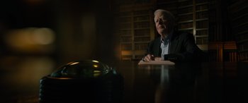 Movie still from “The Pigeon Tunnel” (2023), directed by Errol Morris – An older man sitting at a table in a library; Medium shot, Low angle