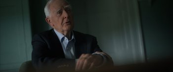 Movie still from “The Pigeon Tunnel” (2023), directed by Errol Morris – An older man sitting at a table with his hands crossed; Close Up shot, Over the shoulder angle