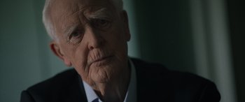 Movie still from “The Pigeon Tunnel” (2023), directed by Errol Morris – An old man in a black suit and white shirt; Close Up shot, Over the shoulder angle