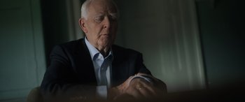 Movie still from “The Pigeon Tunnel” (2023), directed by Errol Morris – An older man in a suit and tie looking down at his wrist; Close Up shot, Over the shoulder angle