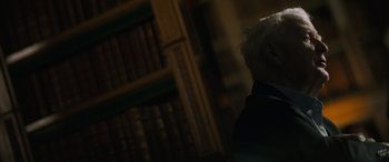 Movie still from “The Pigeon Tunnel” (2023), directed by Errol Morris – An older man in a suit and tie in front of a book shelf; Close Up shot, Over the shoulder angle