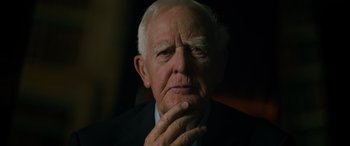 Movie still from “The Pigeon Tunnel” (2023), directed by Errol Morris – An older man in a suit is looking pensive; Close Up shot, Over the shoulder angle