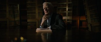 Movie still from “The Pigeon Tunnel” (2023), directed by Errol Morris – An older man sitting at a table in front of a book; Close Up shot, Over the shoulder angle
