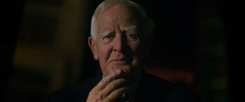 Movie still from “The Pigeon Tunnel” (2023), directed by Errol Morris – An older man in a suit and tie is holding his hand to his face; Close Up shot, Over the shoulder angle