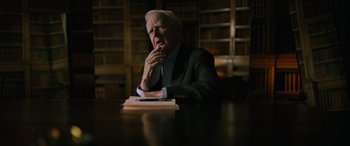 Movie still from “The Pigeon Tunnel” (2023), directed by Errol Morris – An older man sitting at a table in front of a book; Medium shot, Over the shoulder angle