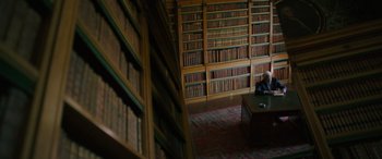 Movie still from “The Pigeon Tunnel” (2023), directed by Errol Morris – A man sitting at a desk in a library; Wide shot, High angle