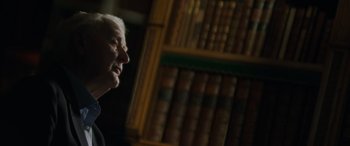 Movie still from “The Pigeon Tunnel” (2023), directed by Errol Morris – An older man sitting in front of a book shelf; Close Up shot, Low angle