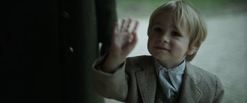 Movie still from “The Pigeon Tunnel” (2023), directed by Errol Morris – A little boy wearing a suit and a tie waving; Close Up shot, Over the shoulder angle