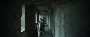 Movie still from “The Pigeon Tunnel” (2023), directed by Errol Morris – A man in prison clothes walking down a hallway; Wide shot, High angle